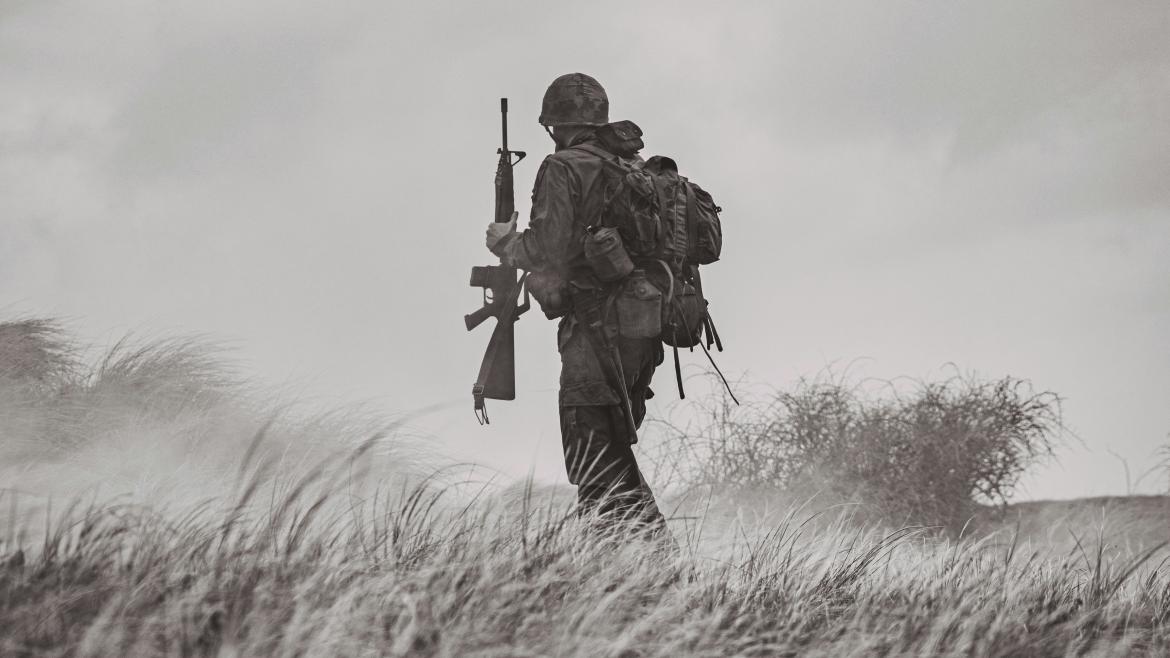 Black and white photo of a soldier standing in a field of tall grass