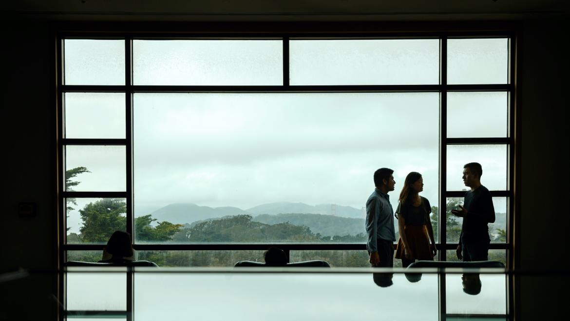 Three individuals talking while standing in front of a large window