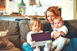 Woman sitting with two small children on a couch while looking at a tablet device