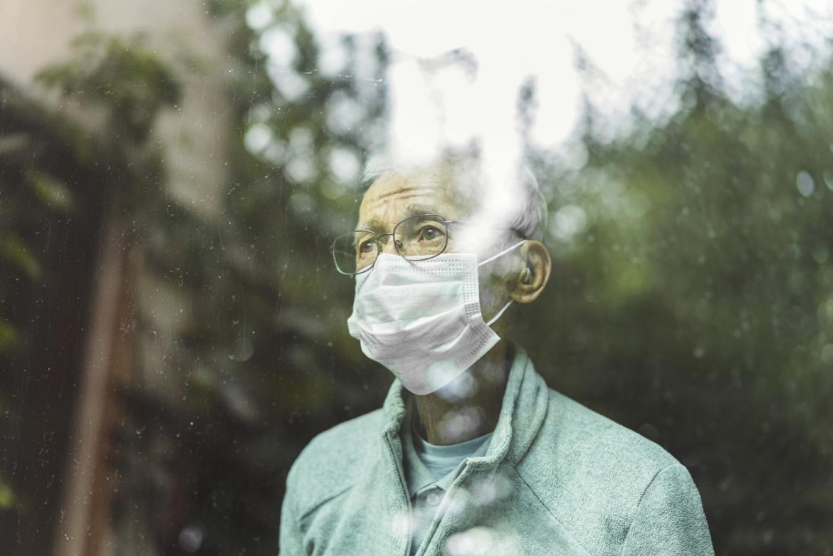 Man looking out a window while wearing a face mask