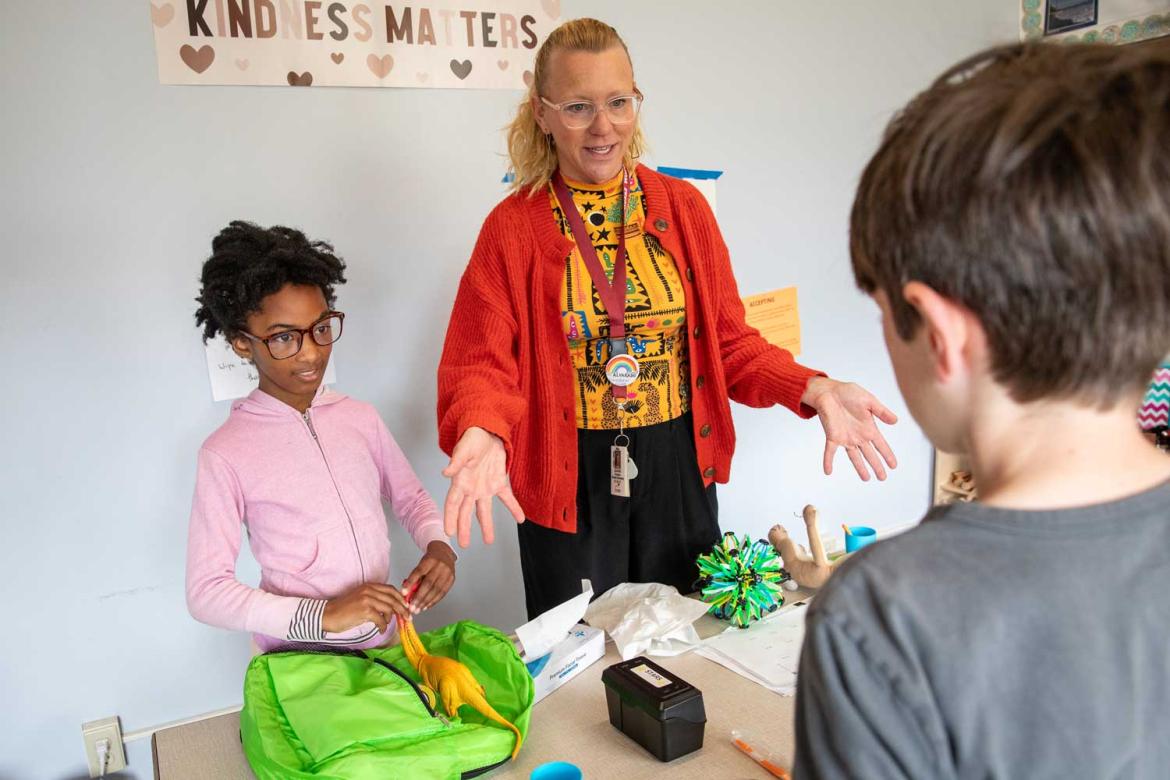 Person with children at a school desk.