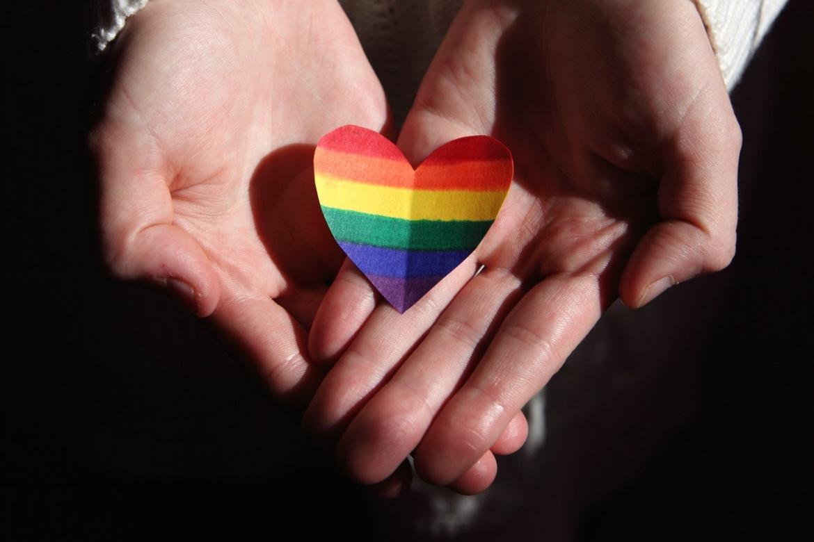 Hands cradling a paper rainbow-colored heart