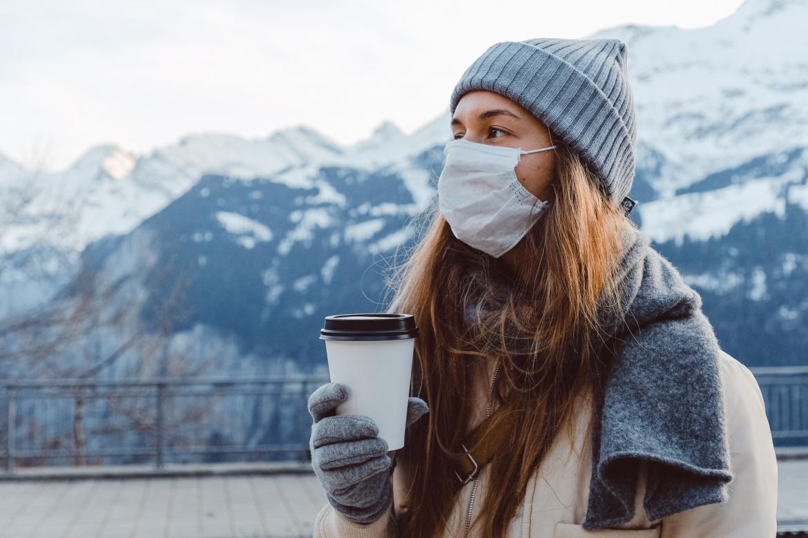 Woman standing outside in the cold while wearing a face mask and holding a disposable cup