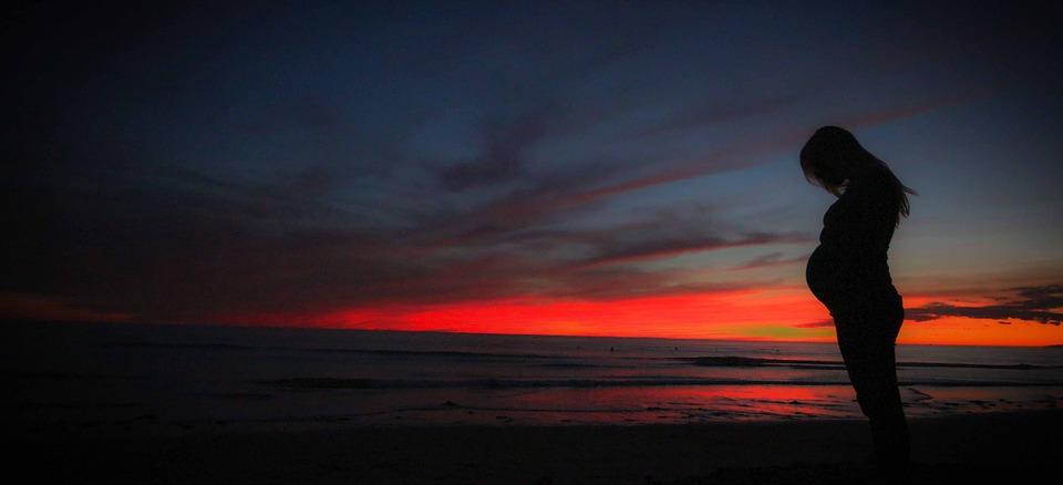 Silhouette of a pregnant woman standing in front of a fading sunset